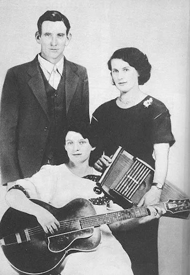 Black-and-white Victor publicity portrait of A. P. Carter, Sara Carter, and Maybelle Carter posed with autoharp and guitar.