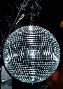 Mirrored disco ball hanging in a dark room and scattering small points of light.