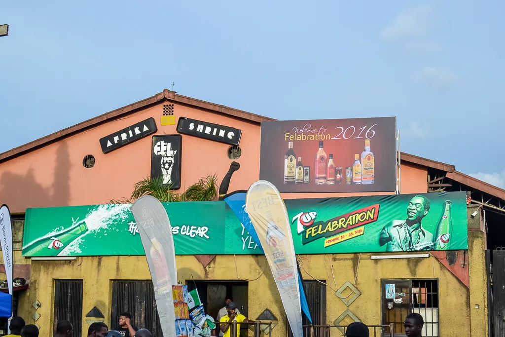 Exterior of the New Afrika Shrine in Lagos, with painted portraits, signs, railings, and people gathered around the entrance.