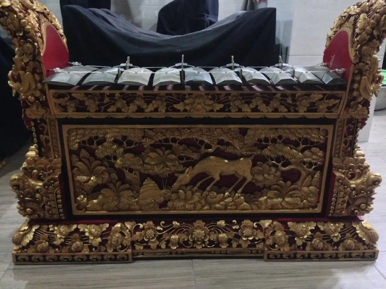 Ten bronze keys hang over bamboo resonators inside the deeply carved wooden case of a Balinese gangsa pemade metallophone.