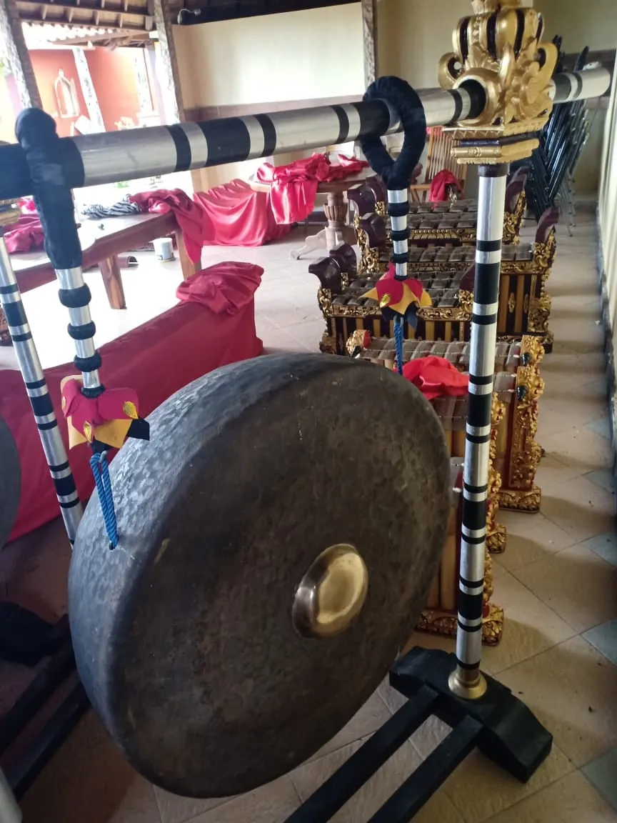 A large dark bronze gong with a raised central boss hangs from a black, red, white, and gold carved frame.