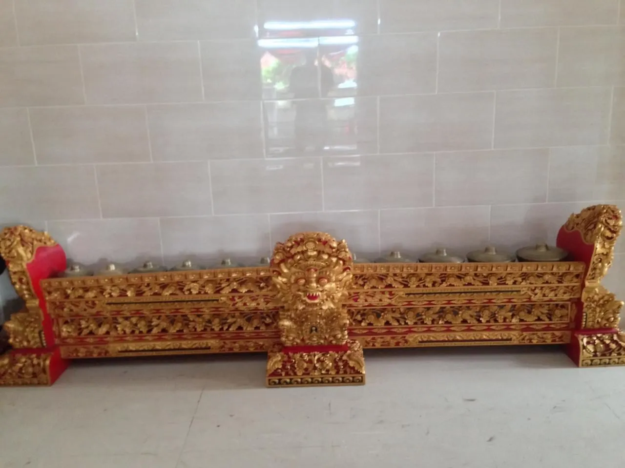 A long carved wooden frame holds a row of small bronze kettle gongs that make up a Balinese reyong.