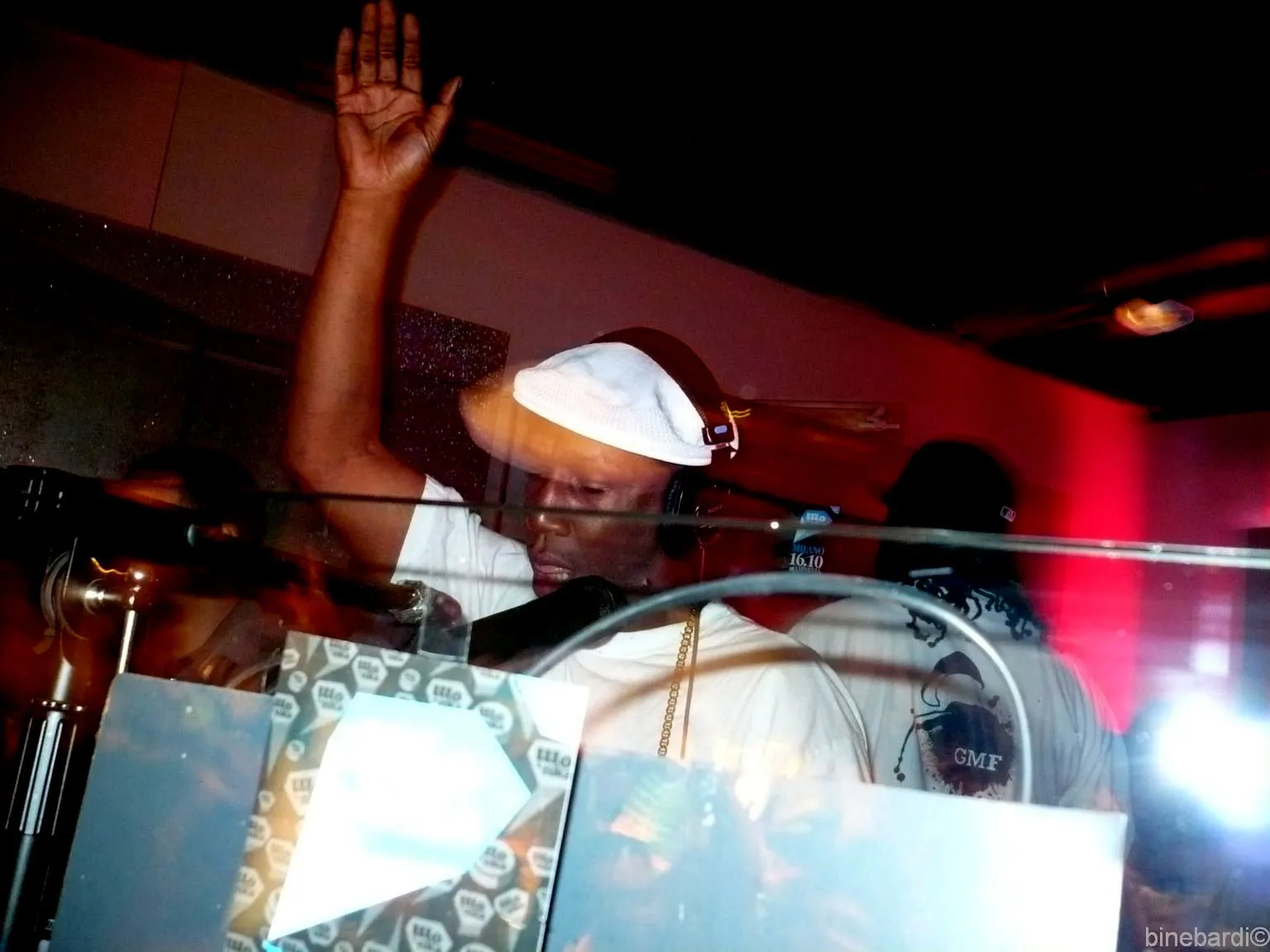 Grandmaster Flash performs with headphones and one hand on a vinyl record while stage lights glow behind the turntables.