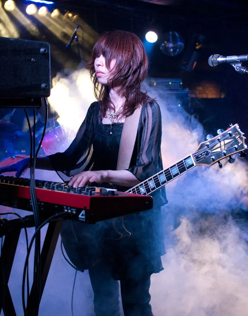 Wata of Boris playing electric guitar onstage beneath blue light, with amplifiers behind her.