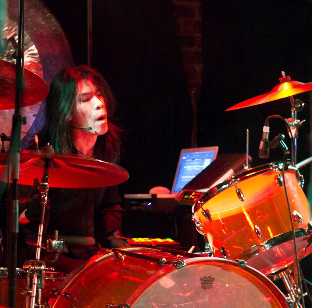 Atsuo of Boris leaning over his drum kit during a live performance under blue stage lighting.