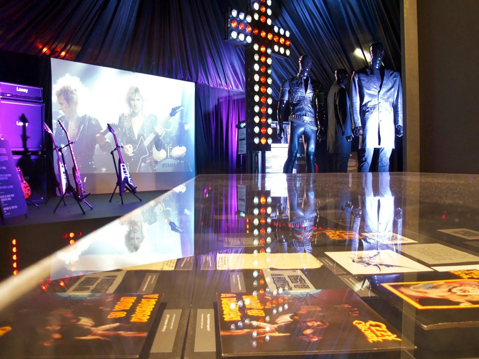 Gallery view of the Home of Metal exhibition at Birmingham Museum and Art Gallery, with stage objects, posters, and a large cross.
