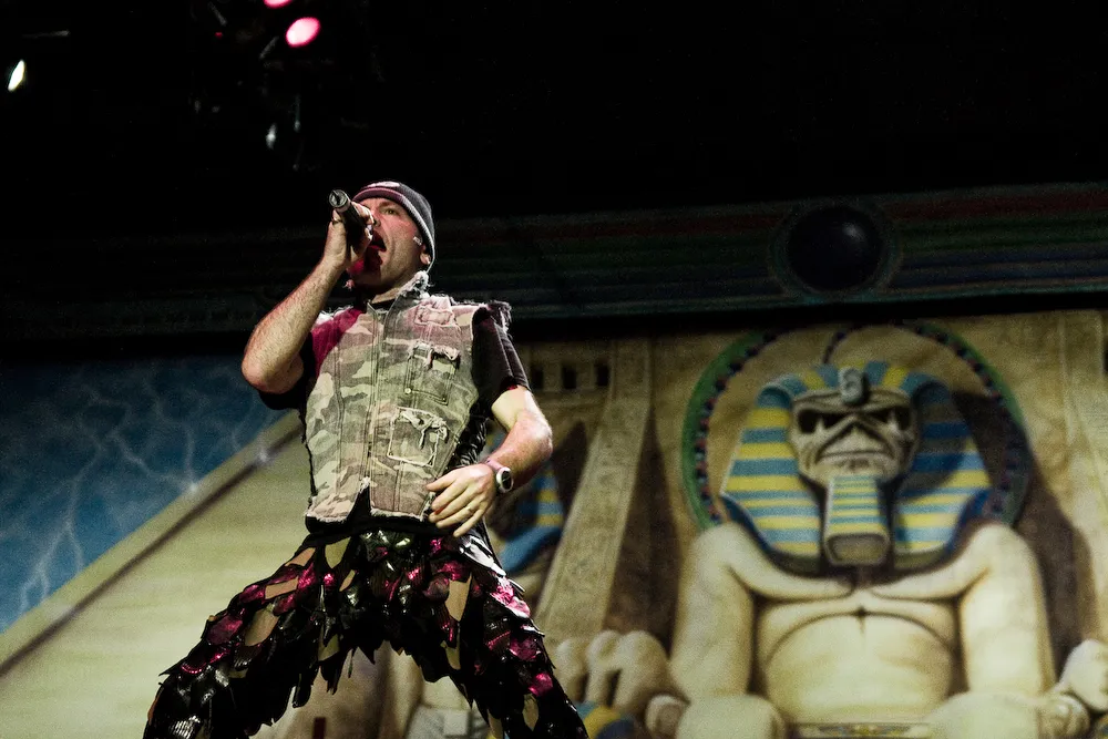 Bruce Dickinson performs with Iron Maiden in 2009, leaning toward a stadium audience beneath bright stage lighting.