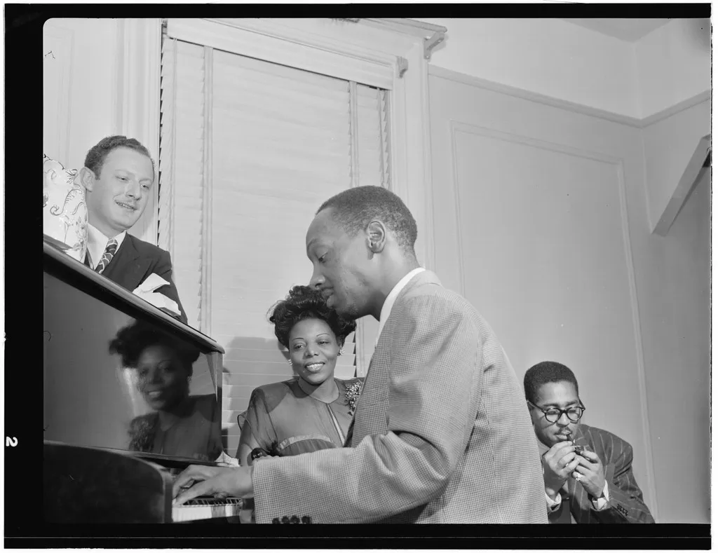 Black-and-white photograph of Milt Orent, Mary Lou Williams, Tadd Dameron, and Dizzy Gillespie gathered in Williams’s New York apartment in 1947.