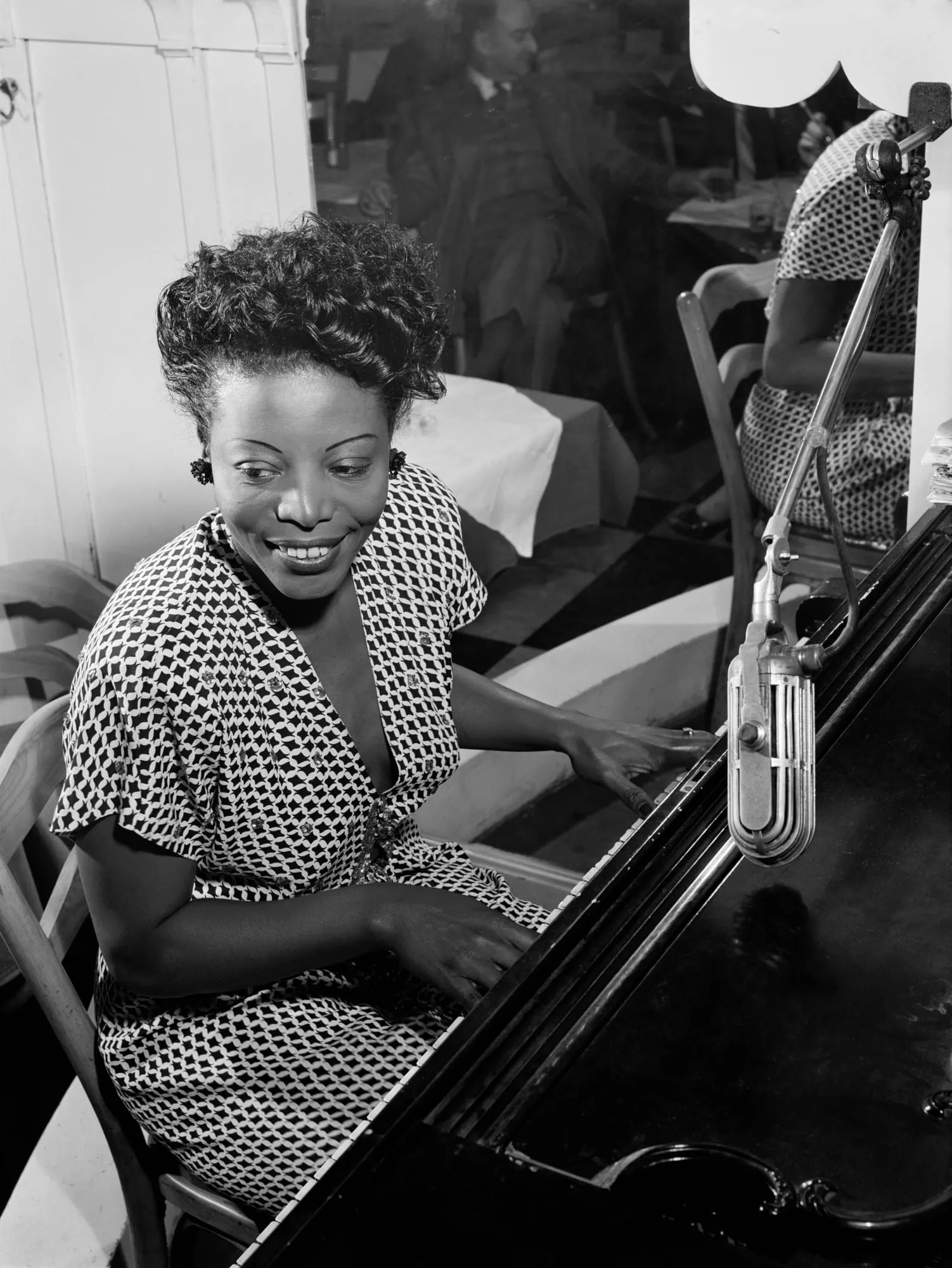 Black-and-white photograph of Mary Lou Williams seated at a piano with both hands on the keys in a New York apartment around 1946.