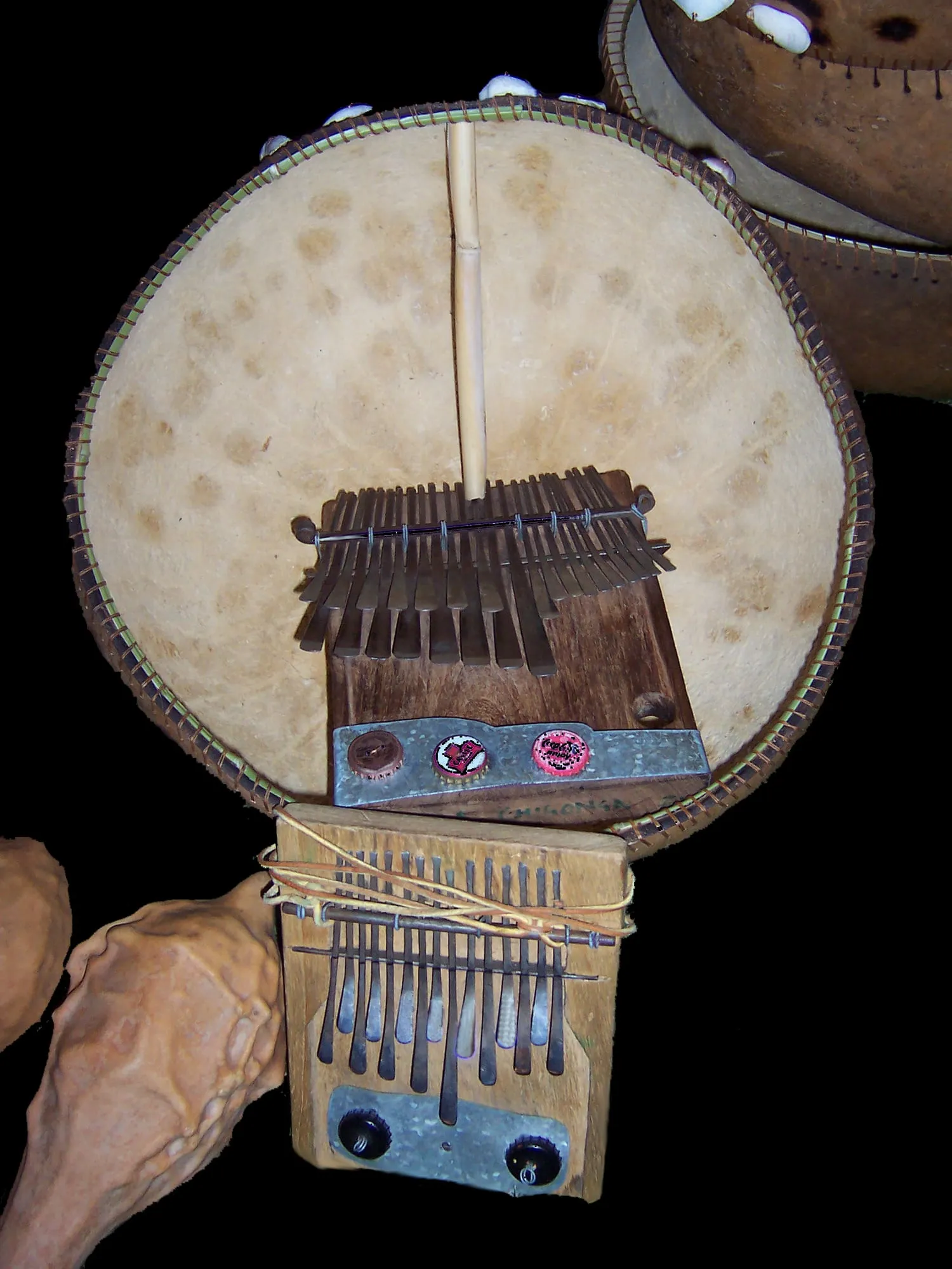 Two differently sized Zimbabwean mbiras, a gourd resonator, and a pair of striped hosho rattles are arranged together on fabric.