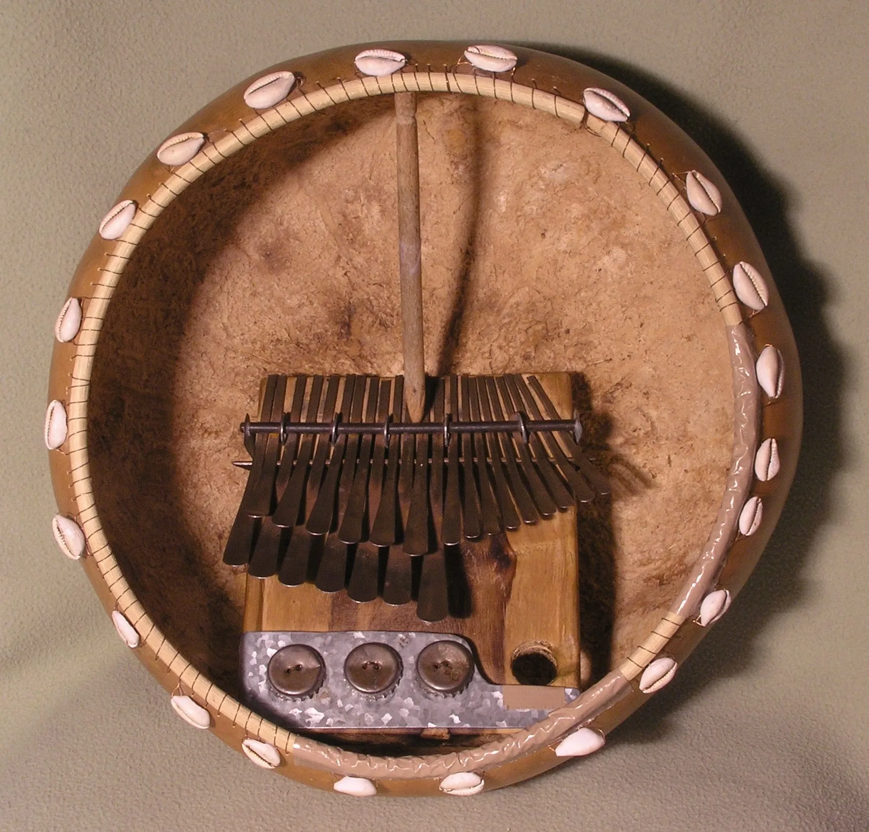 A wooden mbira dza vadzimu rests inside a round brown calabash deze fitted with bottle caps around its outer rim.