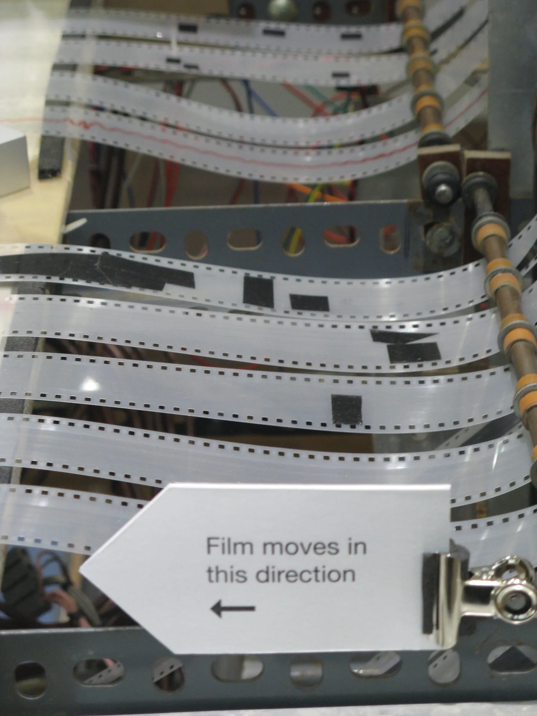 Several parallel strips of perforated film run through the Oramics Machine with hand-applied shapes visible between their edges.
