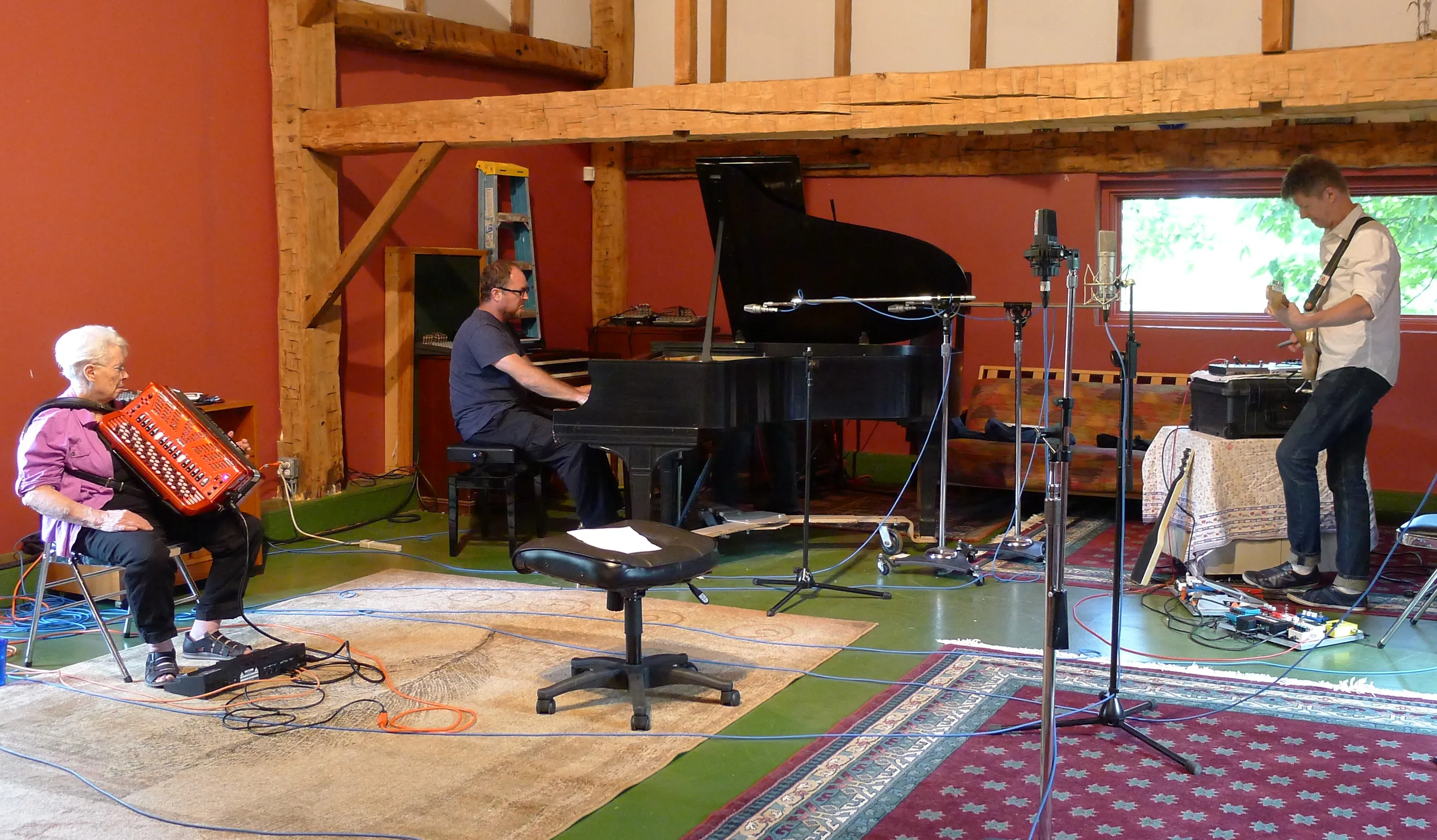 Pauline Oliveros wearing headphones and playing accordion beside Nels Cline and Thollem McDonas during a 2015 recording session.