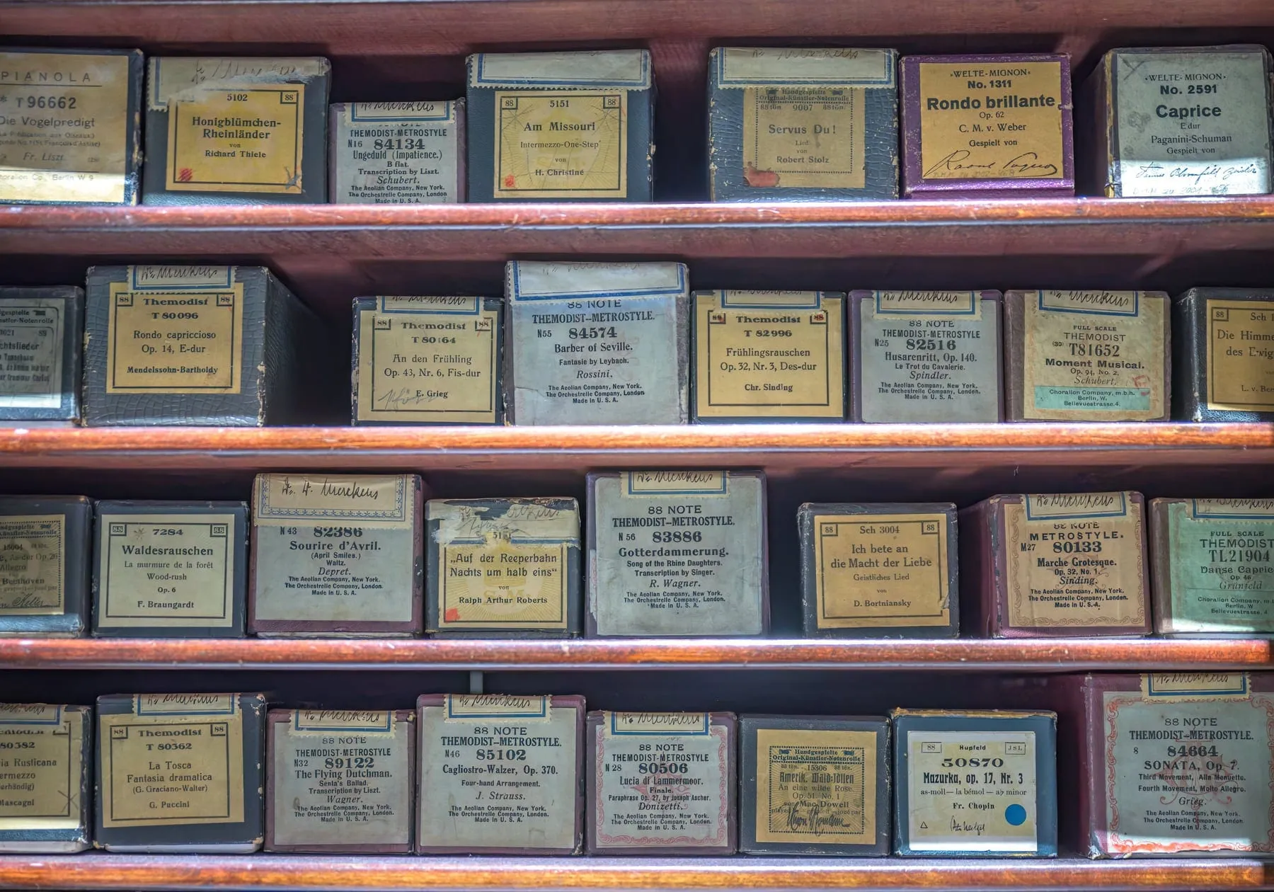 Rows of labeled red, green, blue, and tan piano-roll boxes fill a wooden storage cabinet in the Deutsches Museum collection.