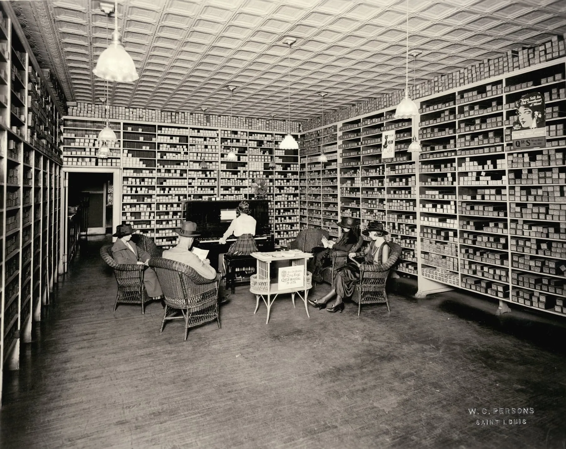 Customers sit at tables inside a 1918 music store whose high walls are covered from floor to ceiling with labeled piano-roll boxes.