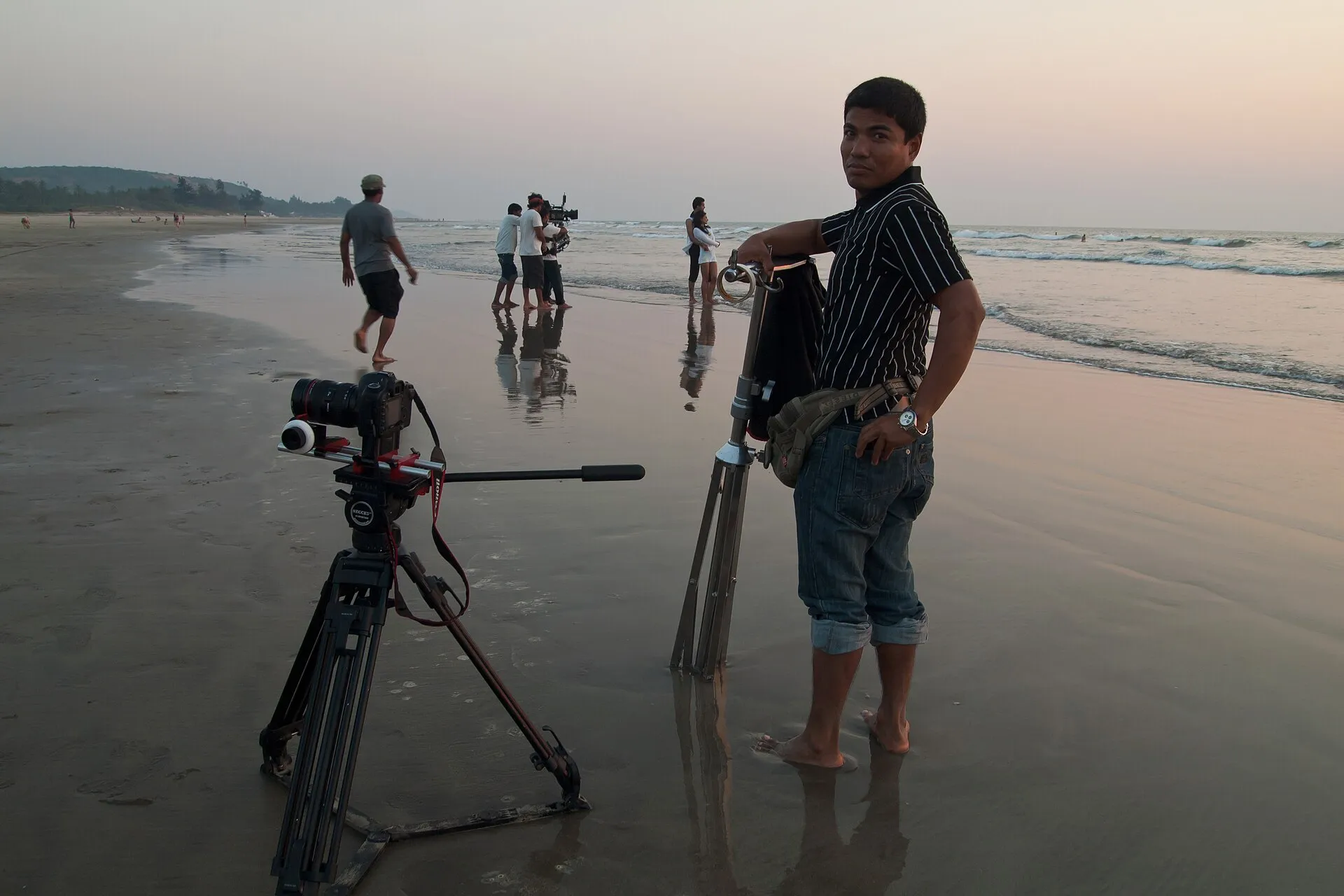 Film crew, camera equipment, performers, and onlookers gathered for a Bollywood production on a beach in Goa.