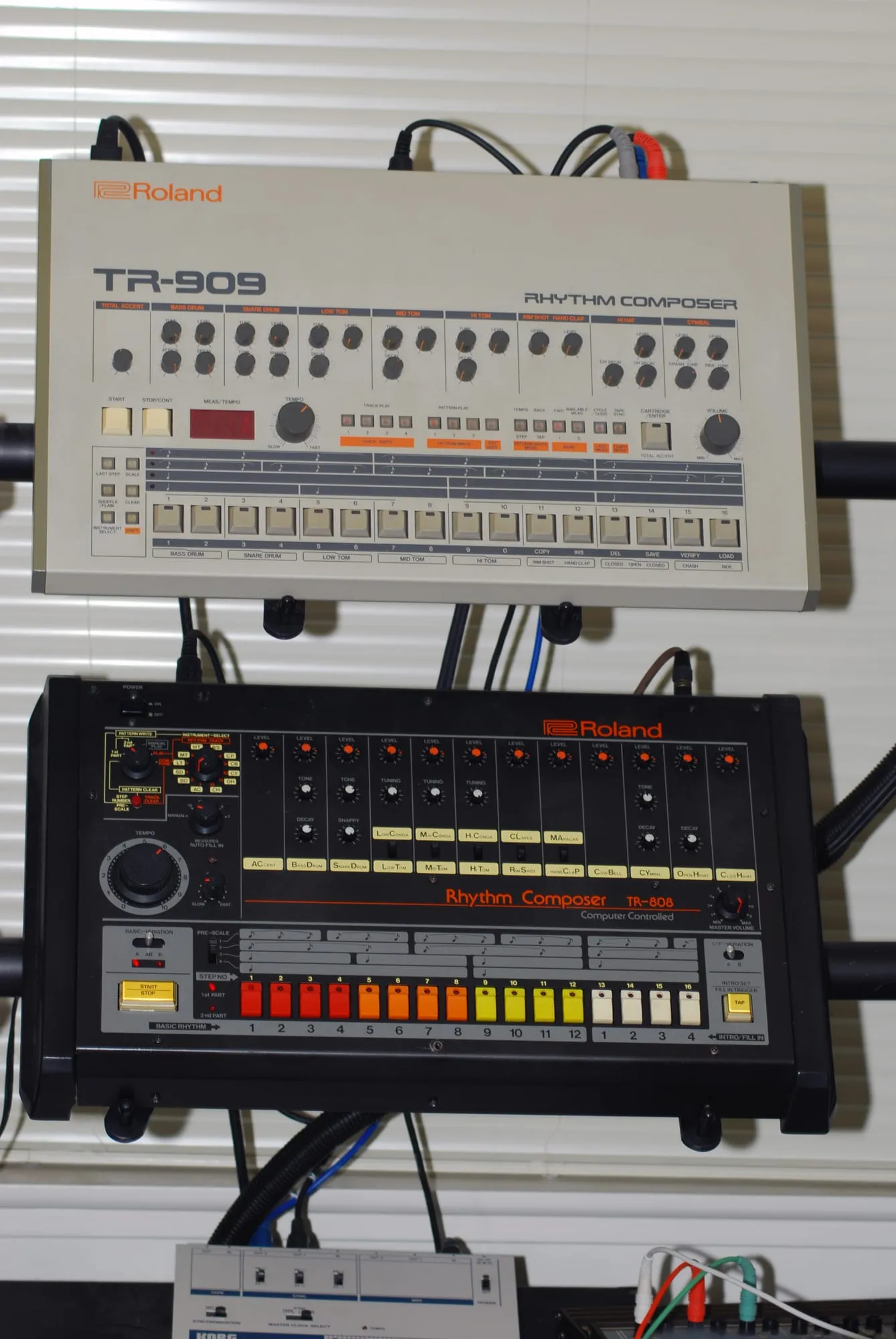 Roland TR-808 and TR-909 drum machines arranged vertically, exposing their knobs, sequencer buttons, labels, and individual outputs.