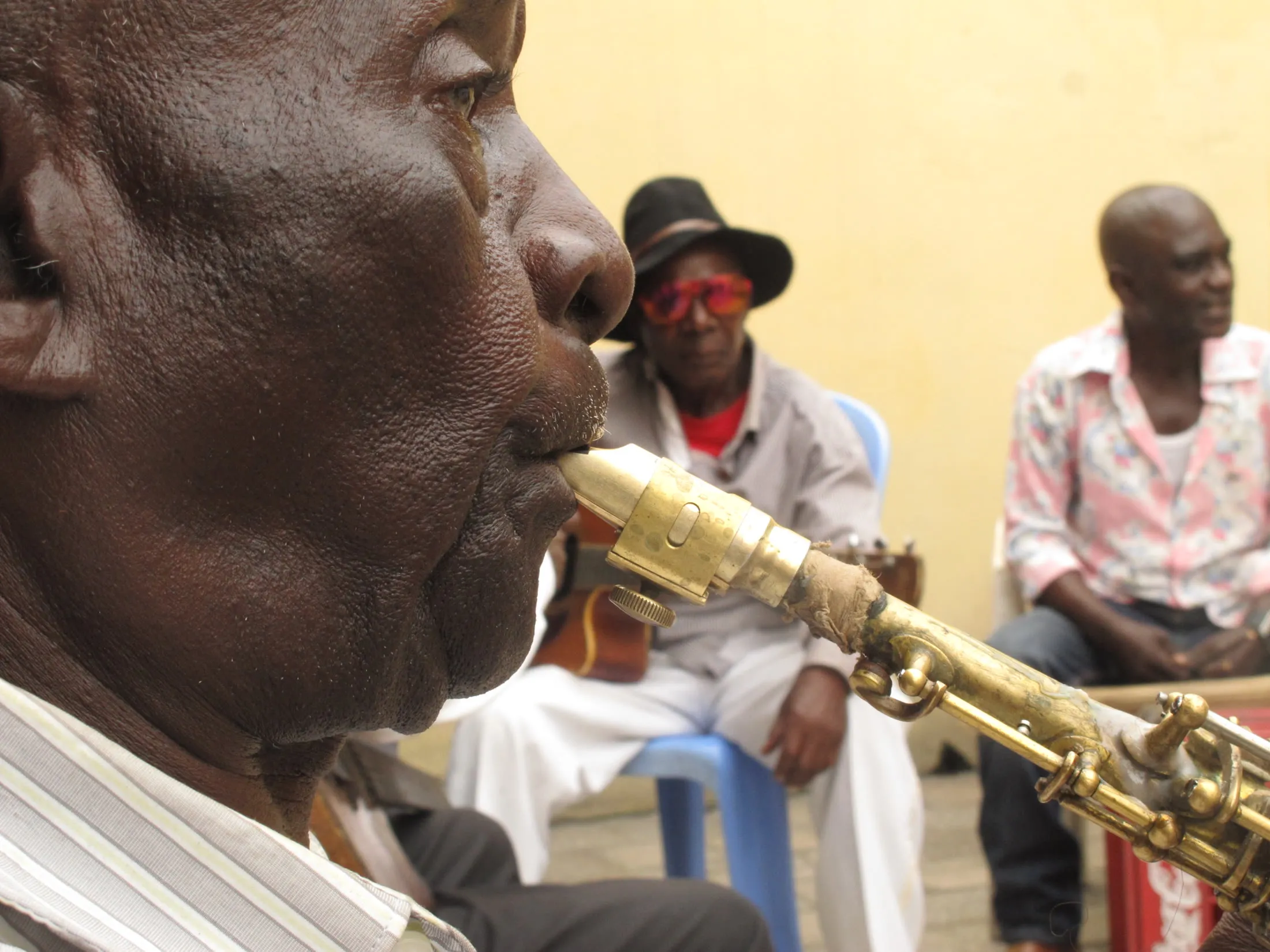 Saxophonist May Plau plays in profile during a Bakolo Music International rehearsal while other musicians sit behind him.