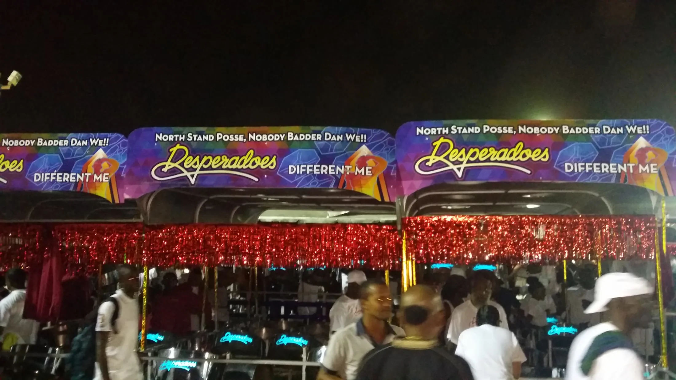 Members of Desperadoes Steel Orchestra stand among wheeled racks of pans during a nighttime rehearsal before the 2016 Panorama finals.