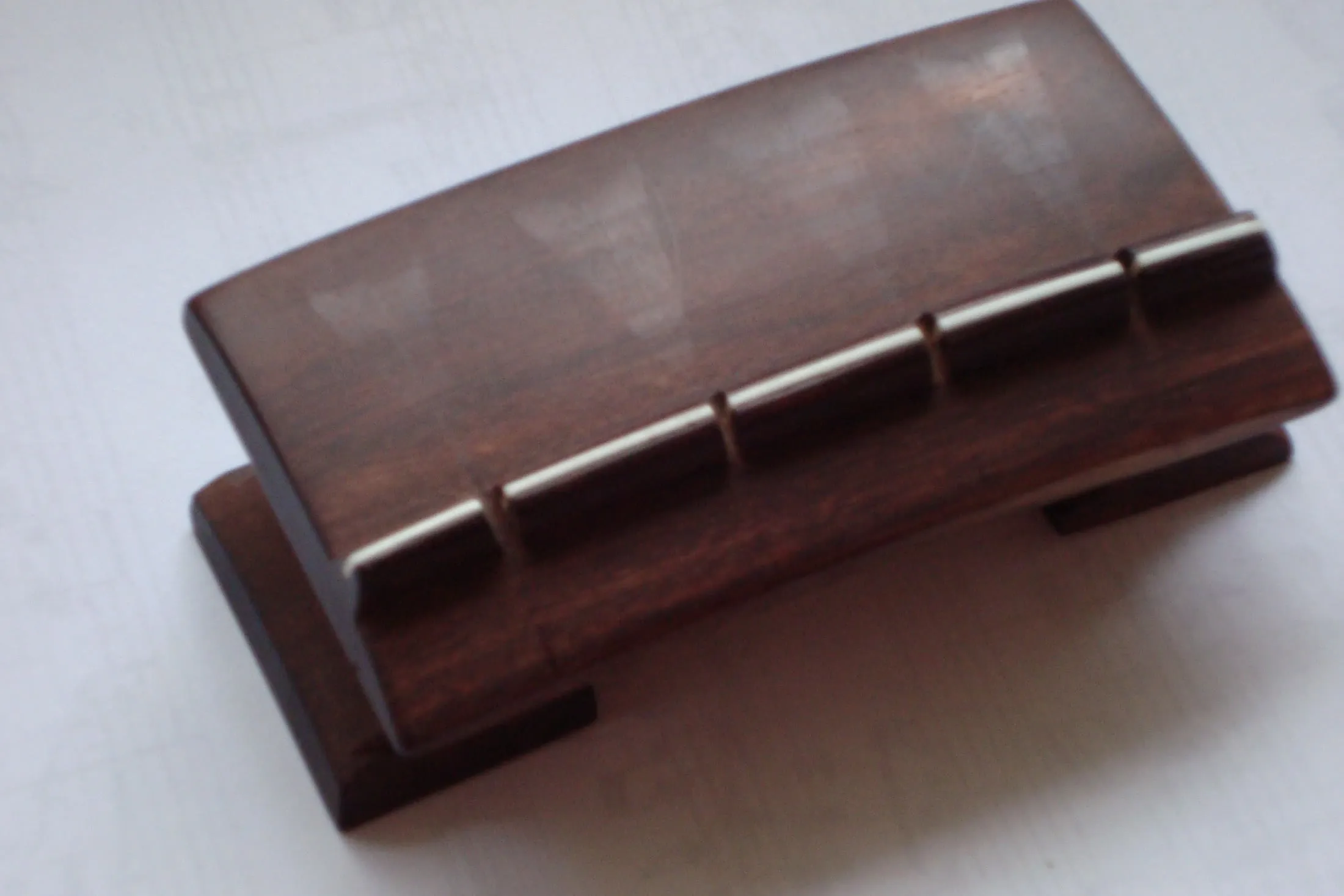 A detached dark rosewood tanpura bridge is photographed from above, showing four shallow paths worn across its broad curved surface.