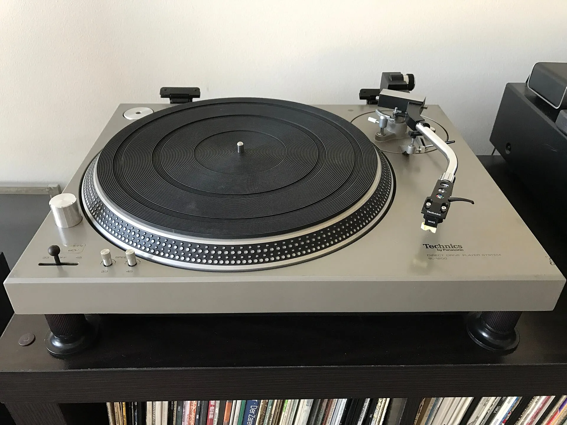 An original silver 1972 Technics SL-1200 turntable is seen from above with its black platter, tonearm, controls, and wooden side panels.