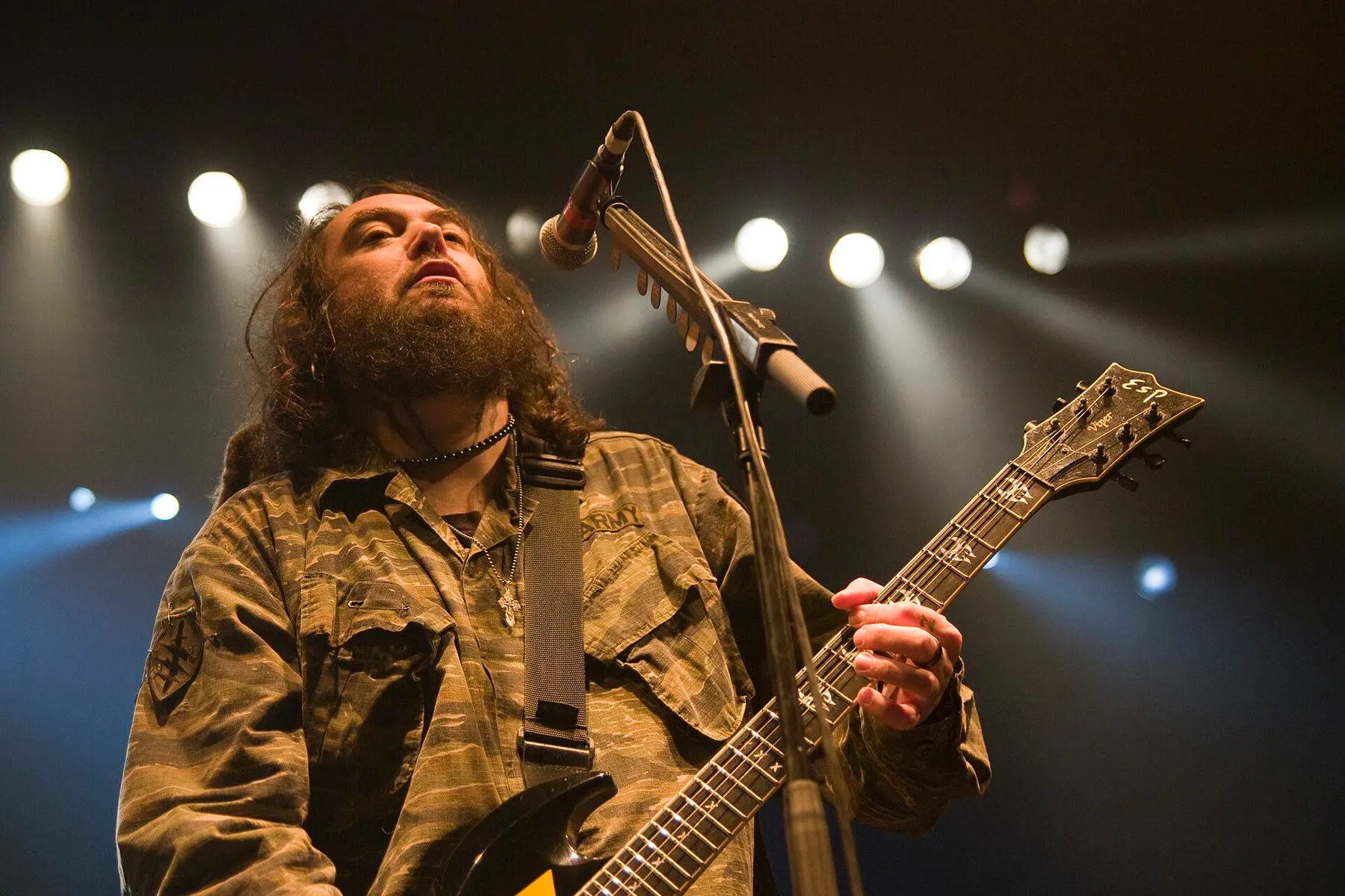 Max Cavalera singing and playing a four-string electric guitar during a 2011 concert.