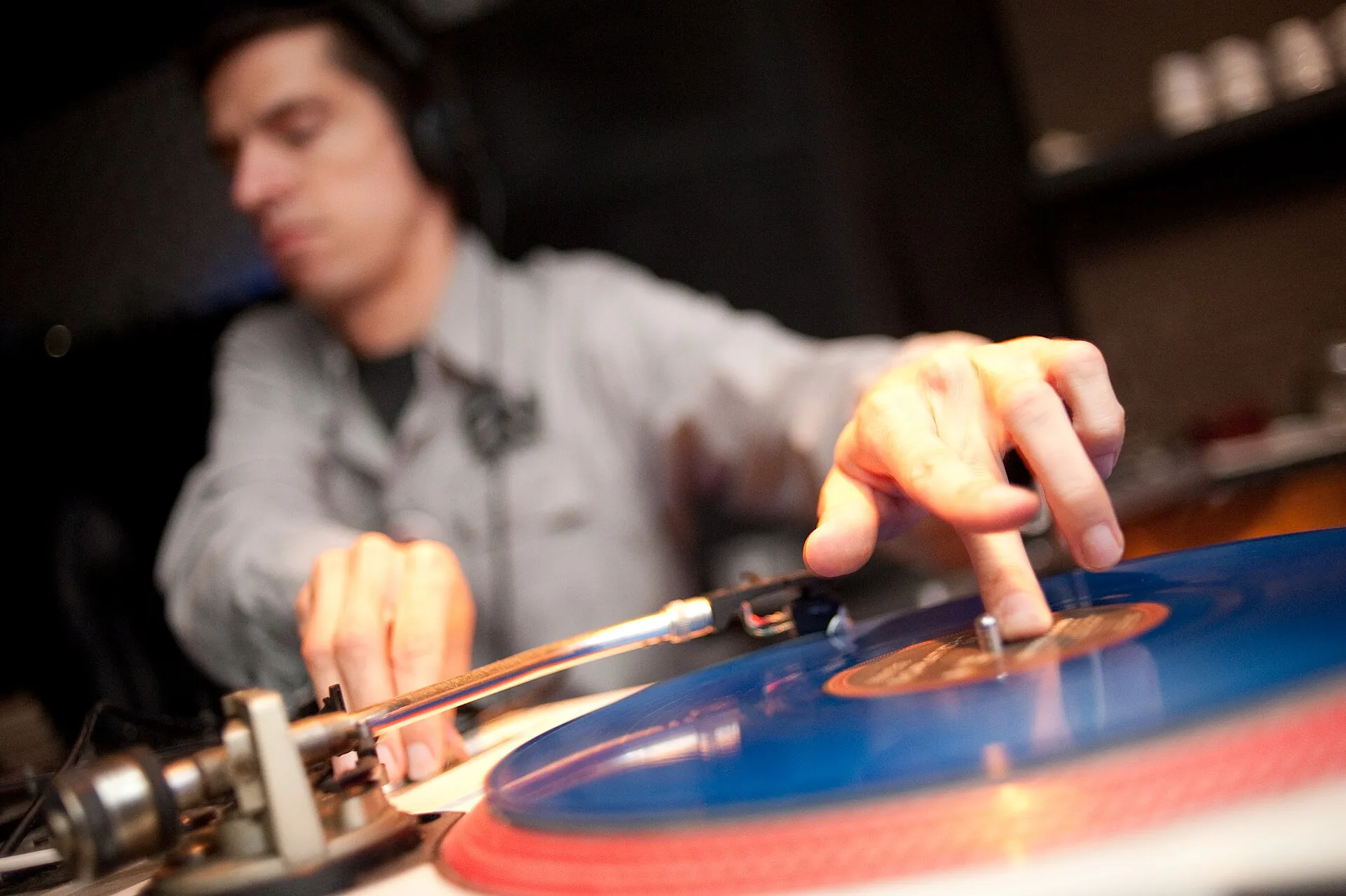 A DJ's hand presses a white-label vinyl record on a turntable beside a mixer during a modern scratching demonstration.