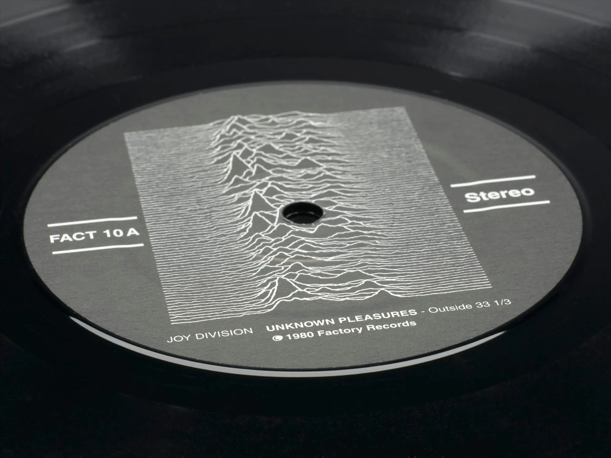 Close museum photograph of the Unknown Pleasures record label with the pulsar plot, FACT 10A number, and stereo marking.
